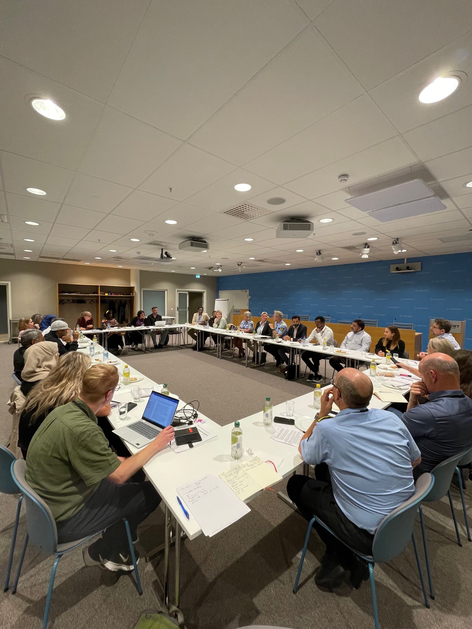 Ulike mennesker som snakker rundt bord plassert i en stor firkant.